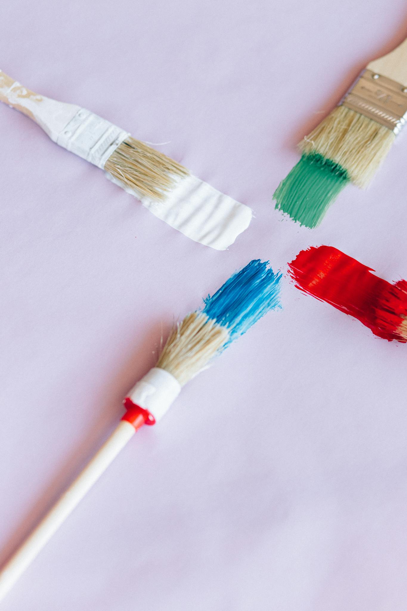 Four paintbrushes with vibrant colors on a light surface.